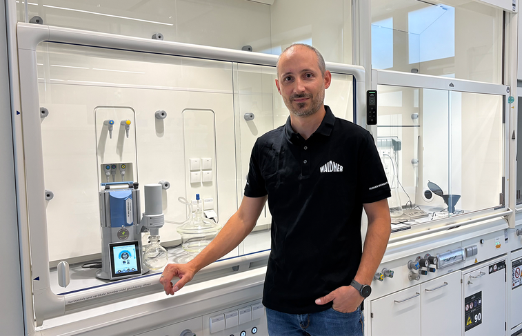 Moriz Walter, Head of Product Development of WALDNER Lab Space Solutions, is standing in front of a laboratory fume hood with a LADS-enabled PC 3001 VARIO select vacuum pump from VACUUBRAND.