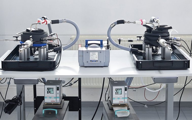 Table with two permeation measuring rigs with a MZ 2C NT vacuum diaphragm pump in the middle.